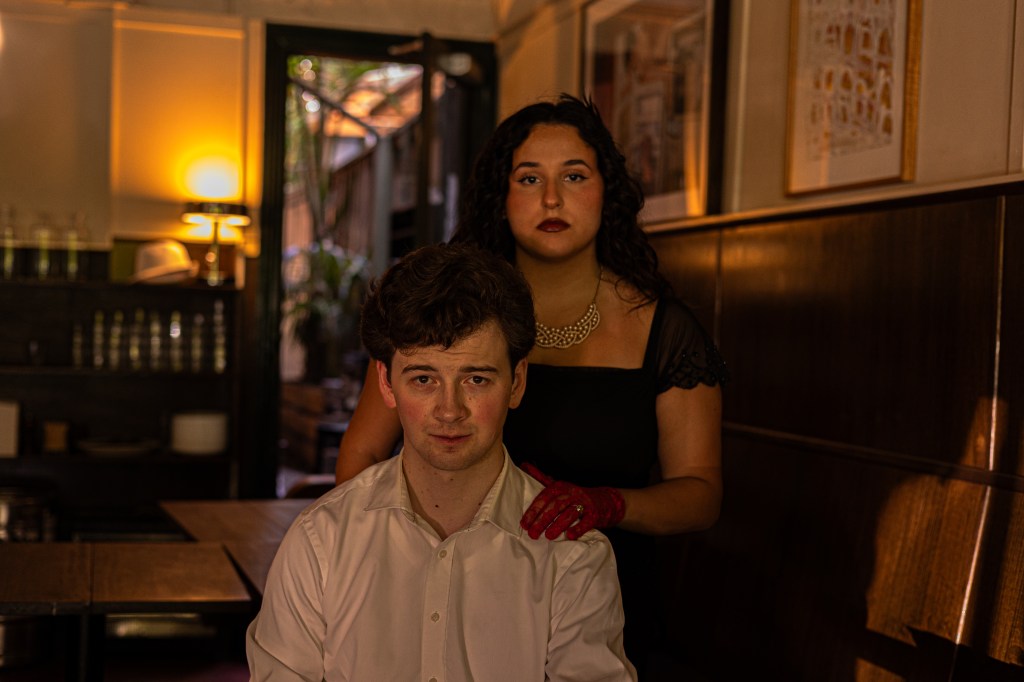 An image of Flynn and Giulia in costume as the Macbeths, Giulia standing behind him with her hand on his shoulder, both looking at the camera.